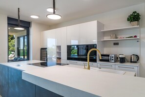 A modern kitchen with a central island, built-in appliances, and a view through a large window. - Villa Jura – Modern Villa with Pool, Wellness and Sea View (Peroj)