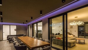 Een moderne eethoek met een lange houten tafel, meerdere stoelen en een glazen scheidingswand.