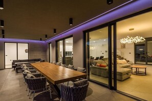 A modern dining area with a long wooden table, multiple chairs, and a glass partition. - Villa Jura – Modern Villa with Pool, Wellness and Sea View (Peroj)