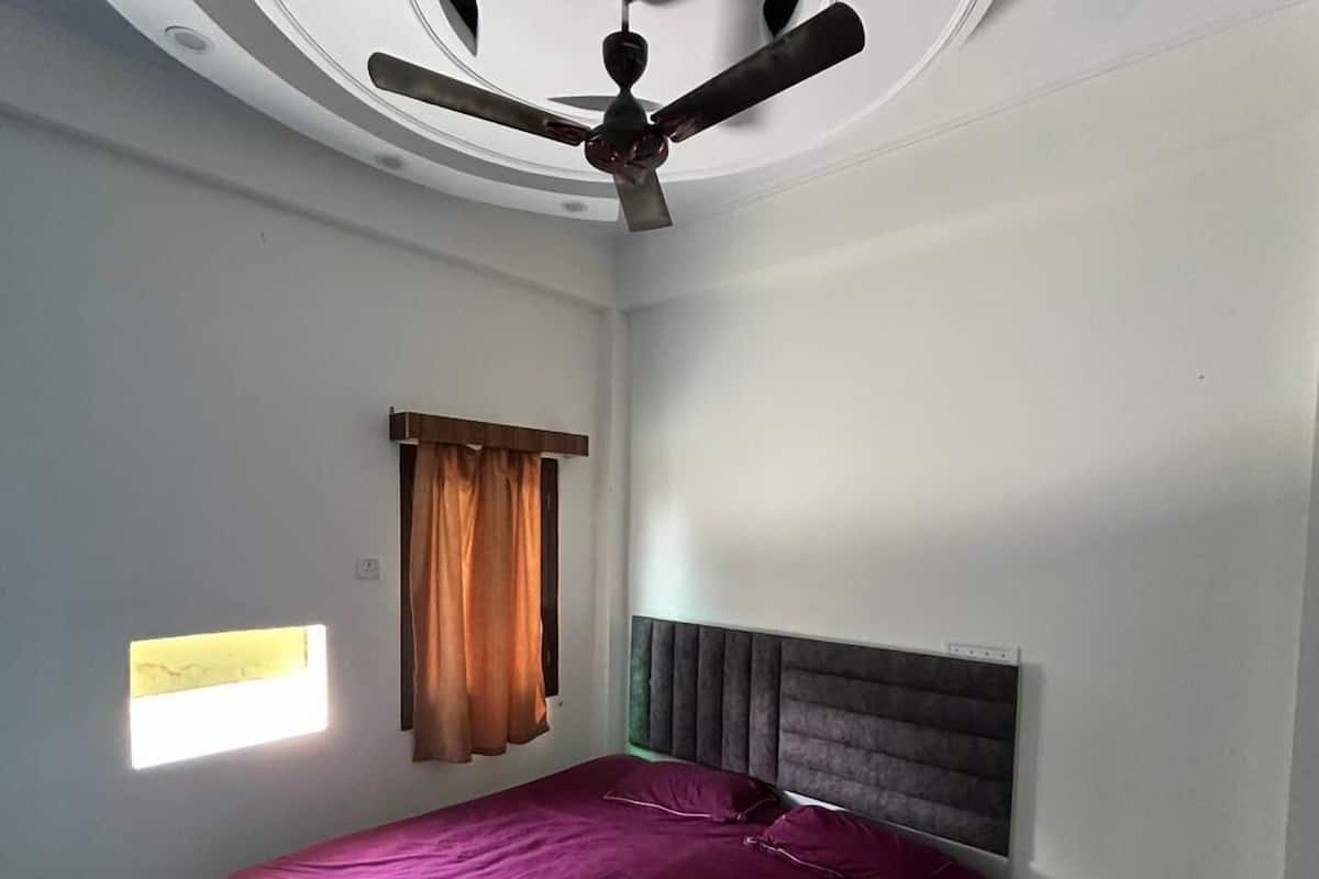 A bedroom with a bed, a ceiling fan, a window with curtains, and a small bedside table.