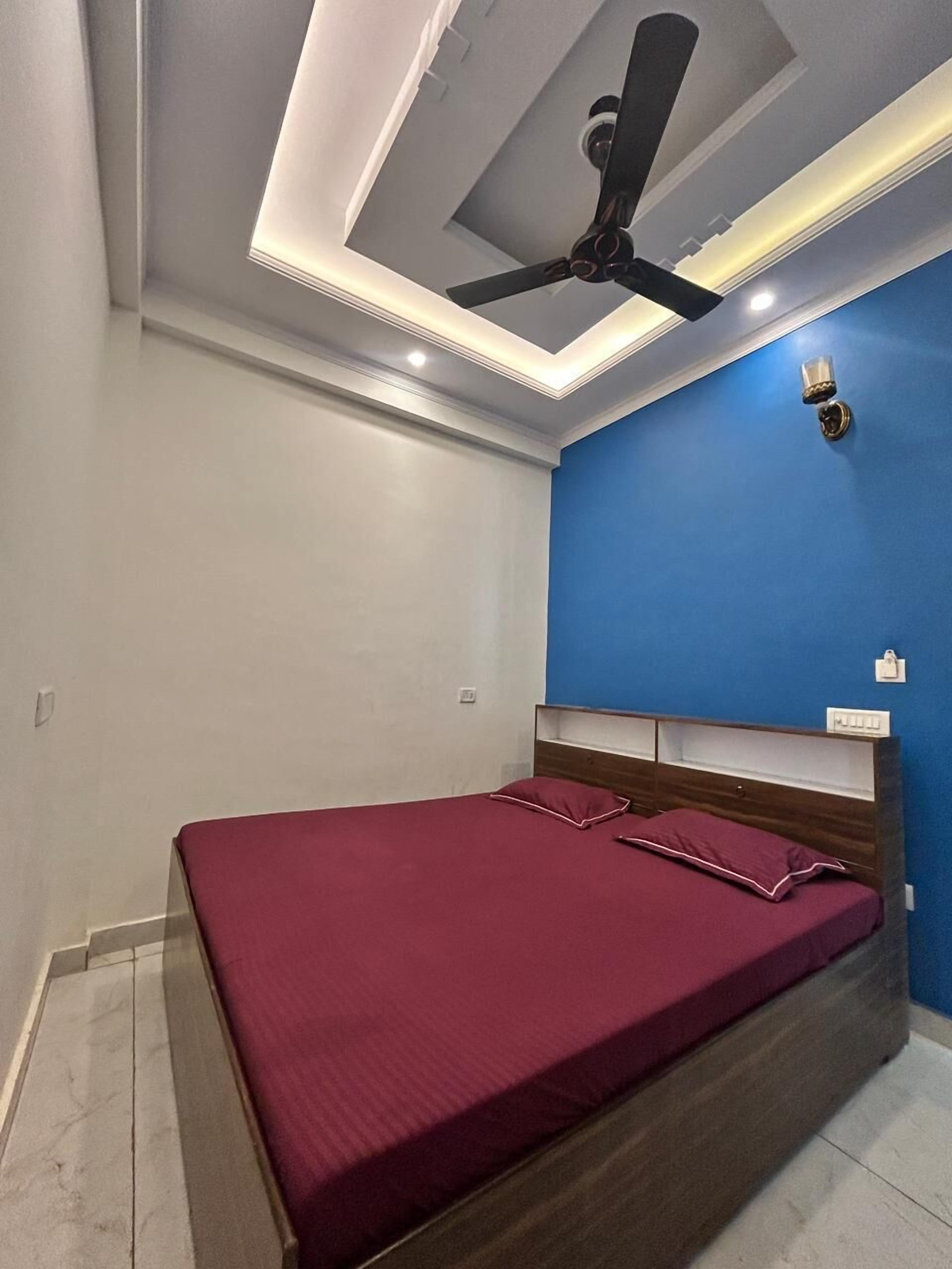 A bedroom with a bed, a ceiling fan, recessed lighting, a blue accent wall, and a wooden headboard.