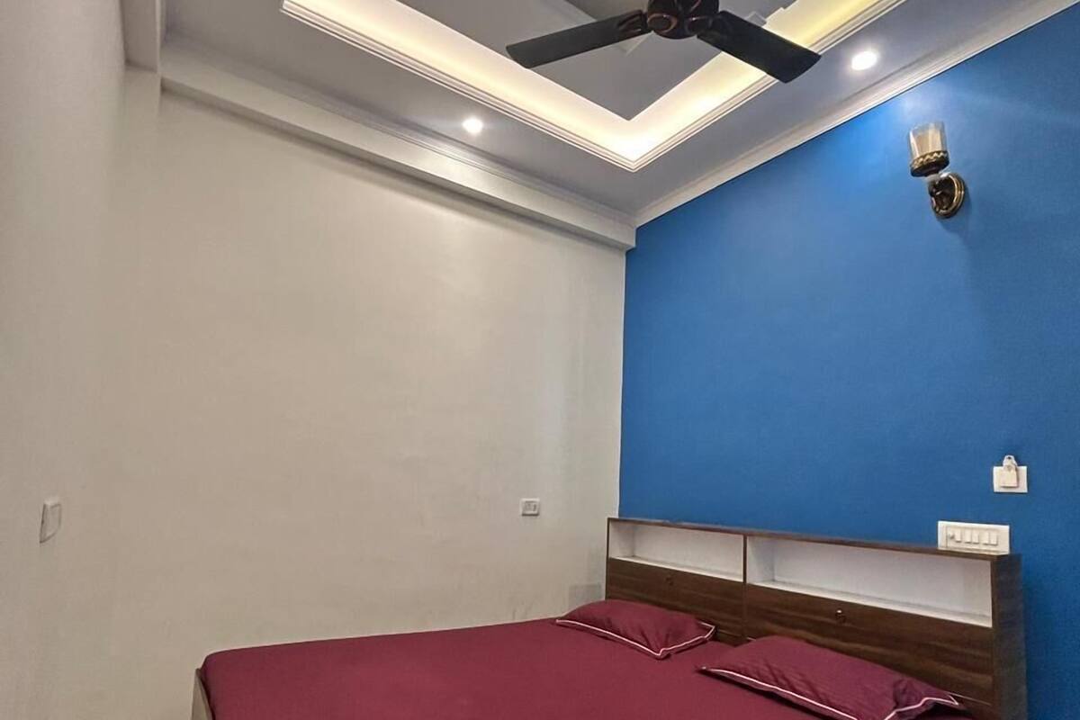 A bedroom with a bed, a ceiling fan, recessed lighting, a blue accent wall, and a wooden headboard.
