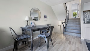 A dining area with a table, chairs, a lamp, a mirror, and a staircase leading to a kitchen. - ADORABLE AND SPACIOUS 2 BR, 2 BA CONDO ... ON REHOBOTH AVE - 18 THE ARK (Rehoboth Beach)