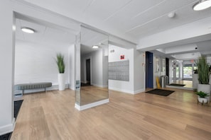 A modern interior with a wooden floor, a glass partition, a bench, potted plants, and a fire alarm on the wall. - ADORABLE AND SPACIOUS 2 BR, 2 BA CONDO ... ON REHOBOTH AVE - 18 THE ARK (Rehoboth Beach)