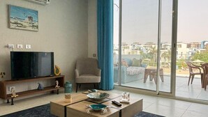 A living room with a TV, a sofa, a chair, a coffee table, and a view of the outside. - Fouka North Coast CL5-TW1-BF (Marsa Matrouh)