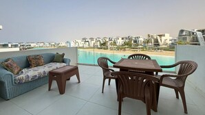 A balcony with a sofa, table, and chairs, overlooking a beach and pool. - Fouka North Coast CL5-TW1-BF (Marsa Matrouh)