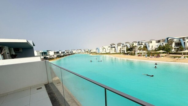 A swimming pool with clear blue water, surrounded by modern buildings and a beach. - Fouka North Coast CL5-TW1-BF (Marsa Matrouh)
