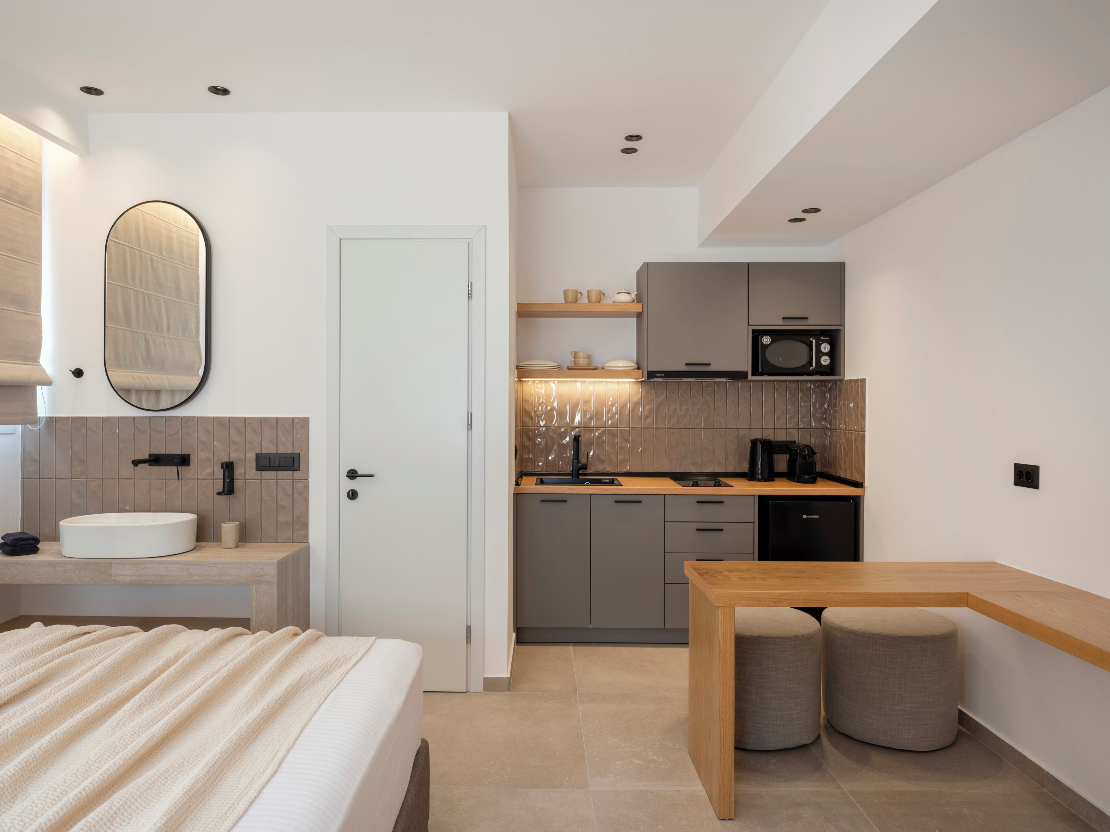 Une chambre d’hôtel moderne équipée d’un lit, d’une table de chevet, d’une petite kitchenette et d’une salle de bain.
