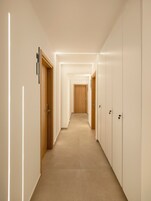 Un pasillo con puertas a ambos lados, una puerta de madera al final y una tira de luz en la pared.