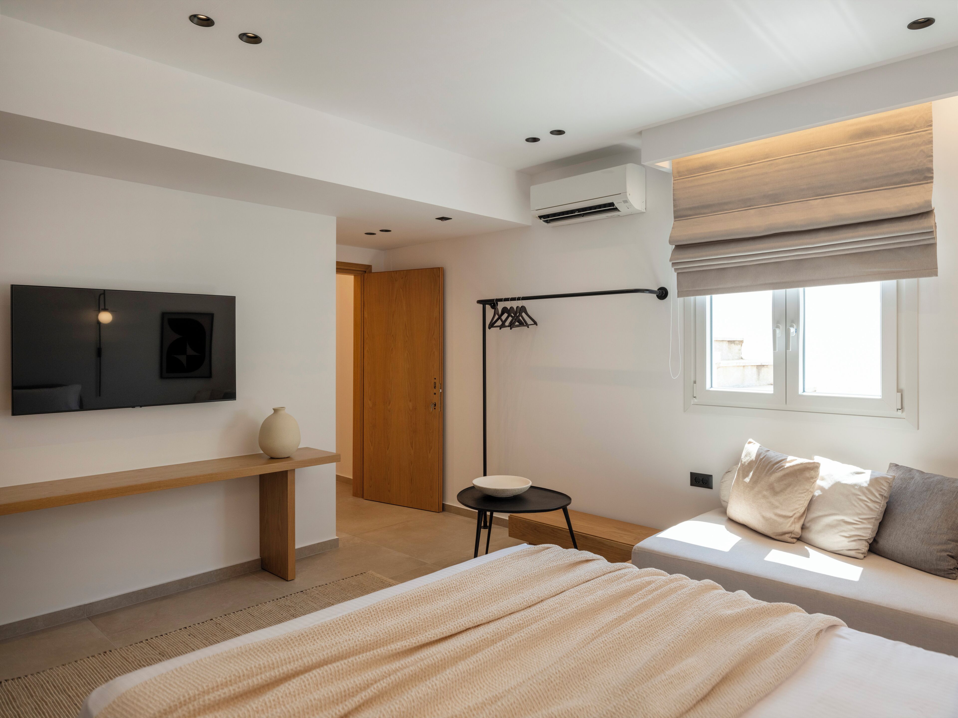 Une chambre à coucher moderne, équipée d’un lit, d’une table de chevet, d’un téléviseur fixé au mur, d’une fenêtre avec des stores et d’un appareil de climatisation.