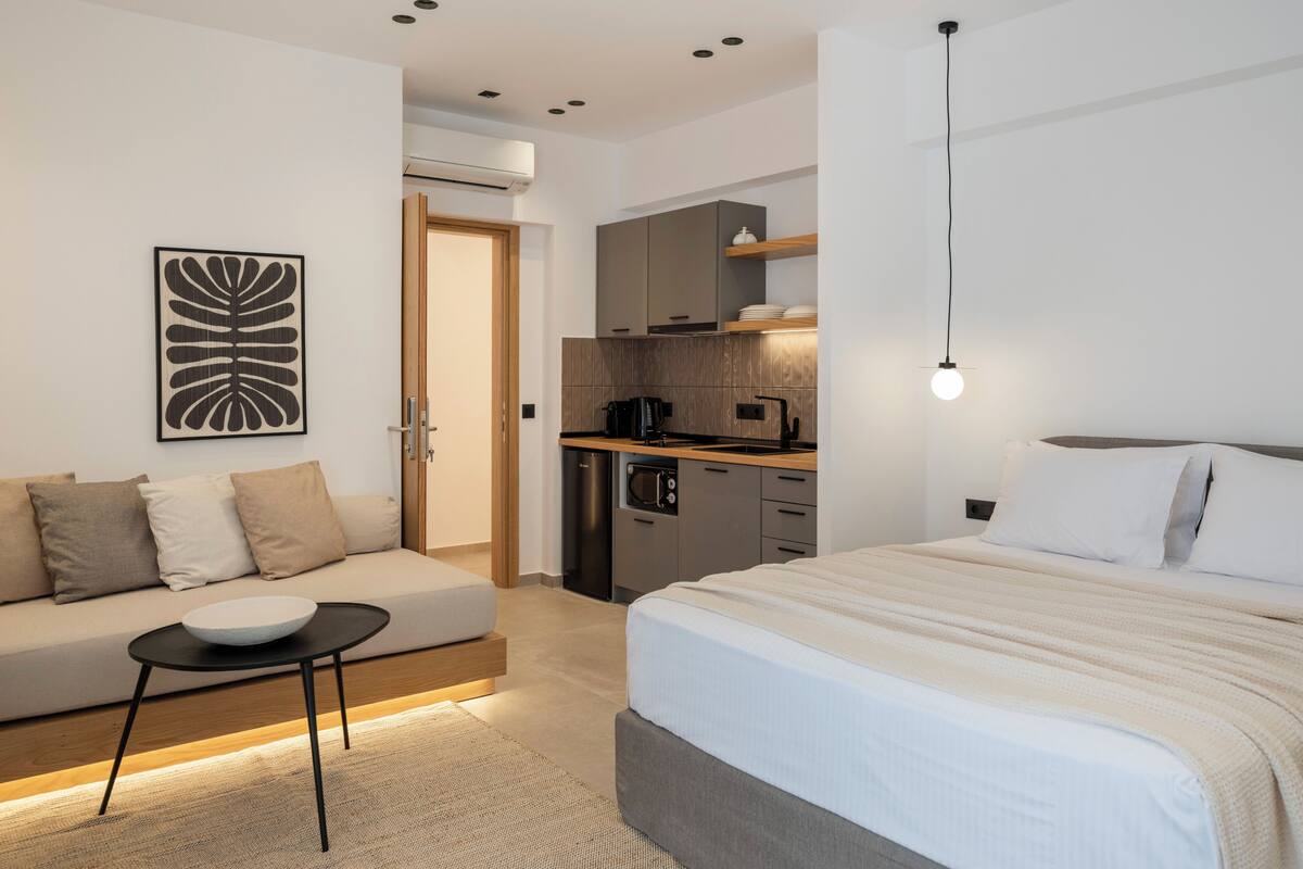 Ein modernes Hotelzimmer mit Bett, einer Couch, einem kleinen Tisch, einer Küchenzeile und einer Wandleuchte.