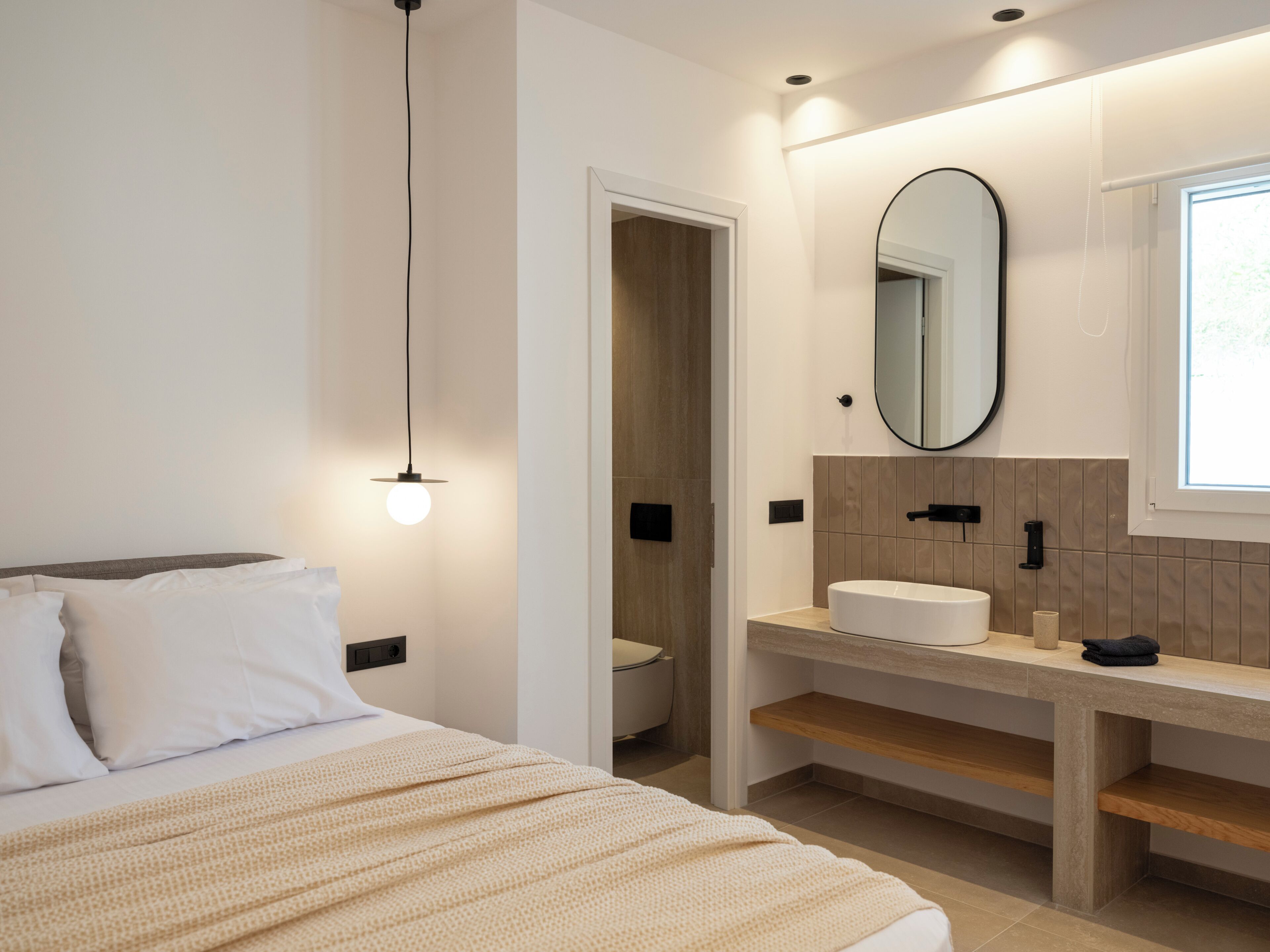 Ein modernes Schlafzimmer mit Bett, Nachttischlampe und einem Badezimmer mit Waschbecken und Spiegel.