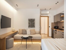 Una habitación de hotel moderna con sofá, una mesita, un televisor de pantalla plana, una obra de arte en la pared y una kitchenette.