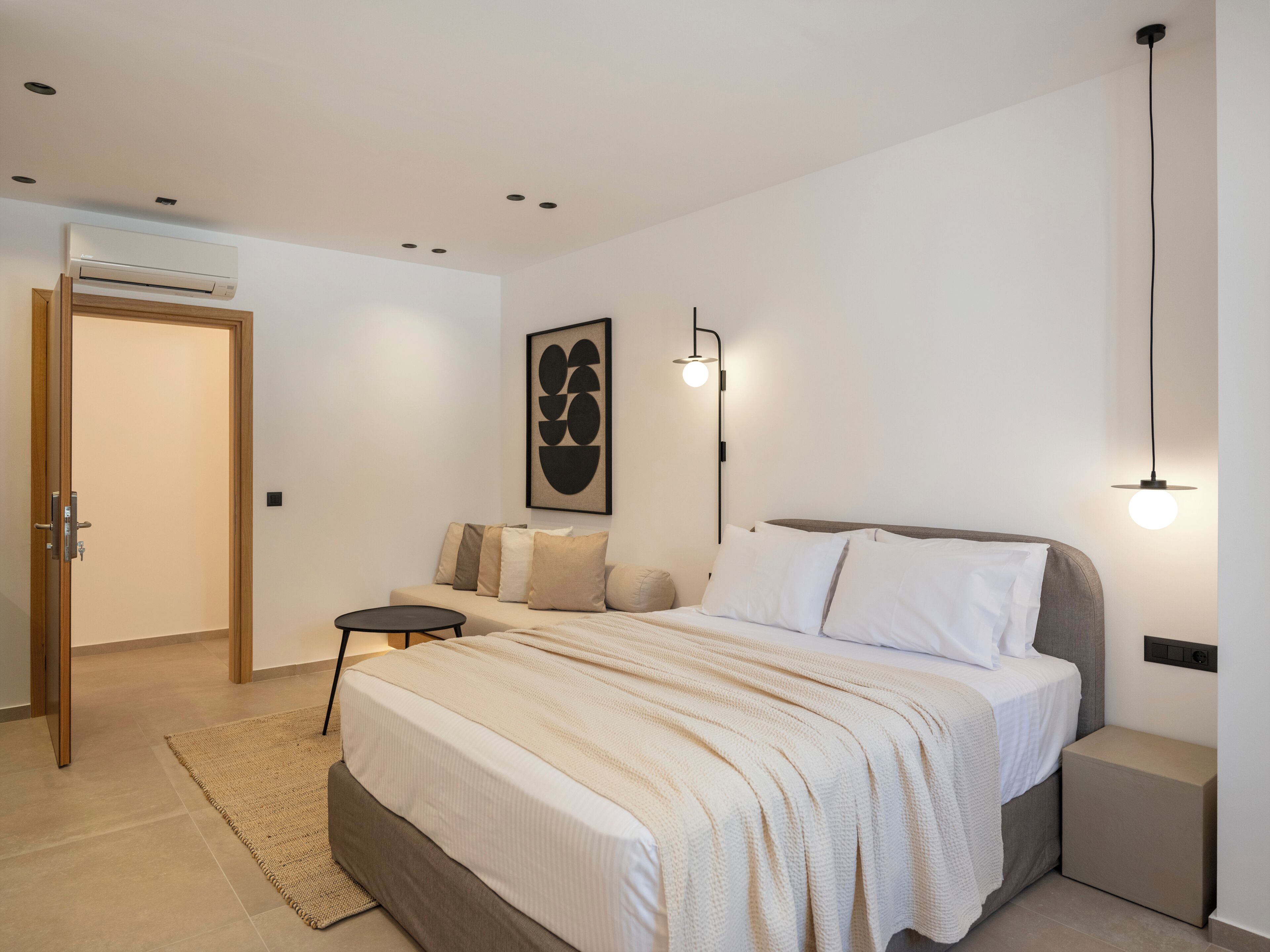 A modern bedroom with a bed, bedside tables, a wall-mounted light, and a door.