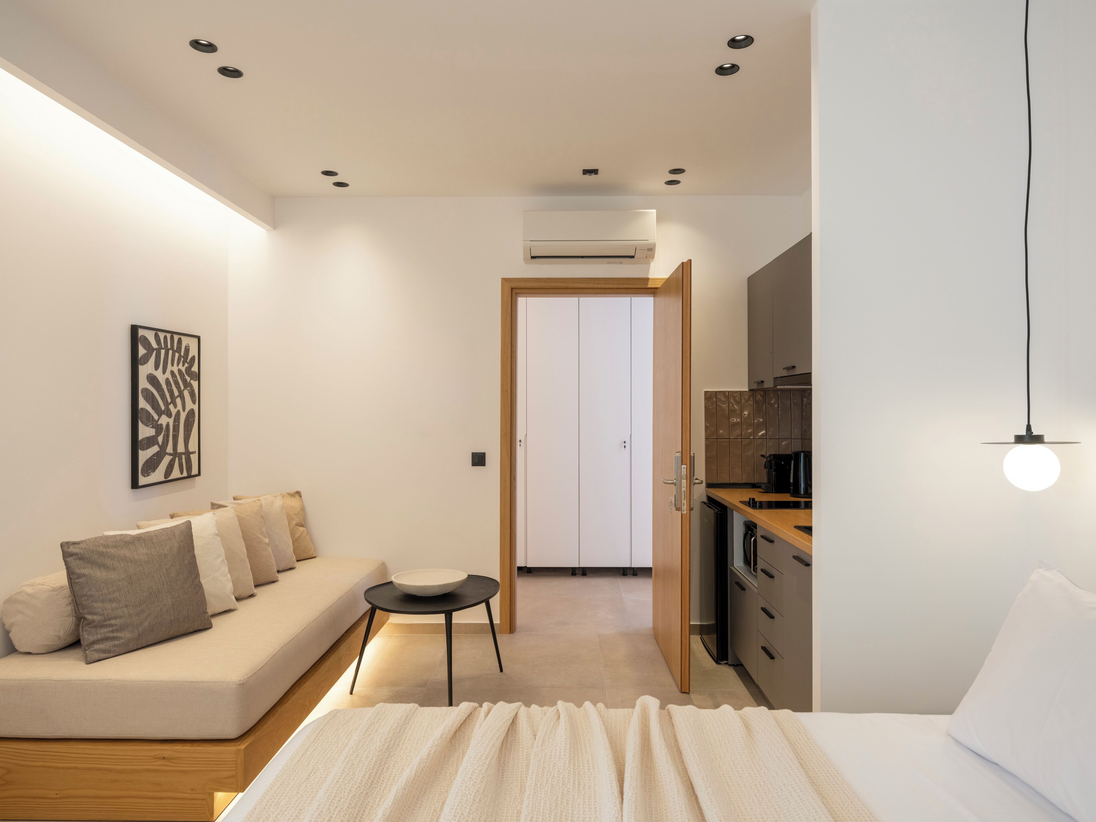 Un dormitorio moderno con una cama, una mesita, un sofá y una kitchenette.