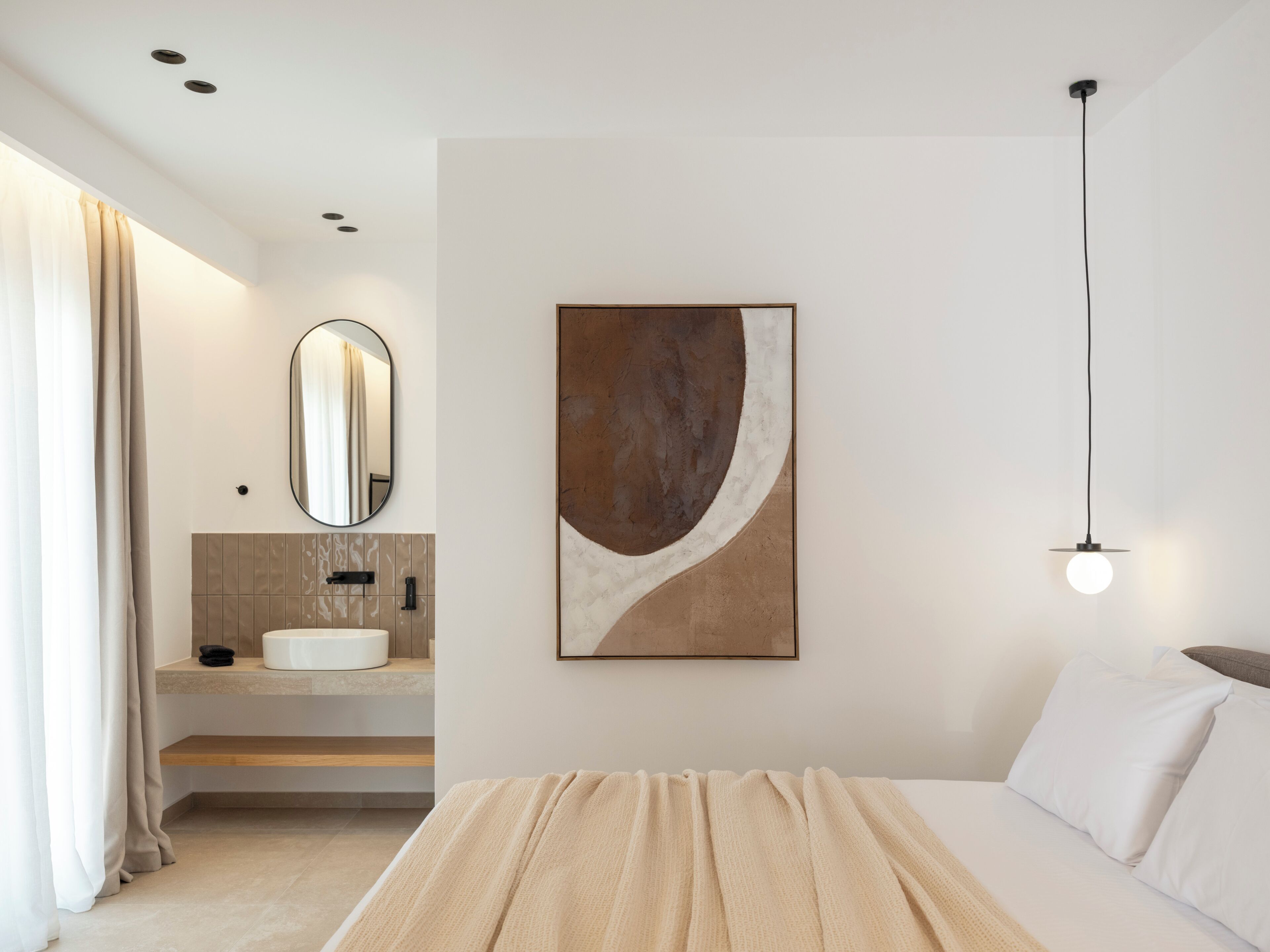 A modern bedroom with a bed, a bedside table, a mirror, a sink, and a wall-mounted artwork.