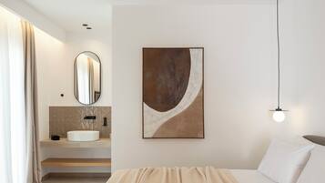 A modern bedroom with a bed, a bedside table, a mirror, a sink, and a wall-mounted artwork.