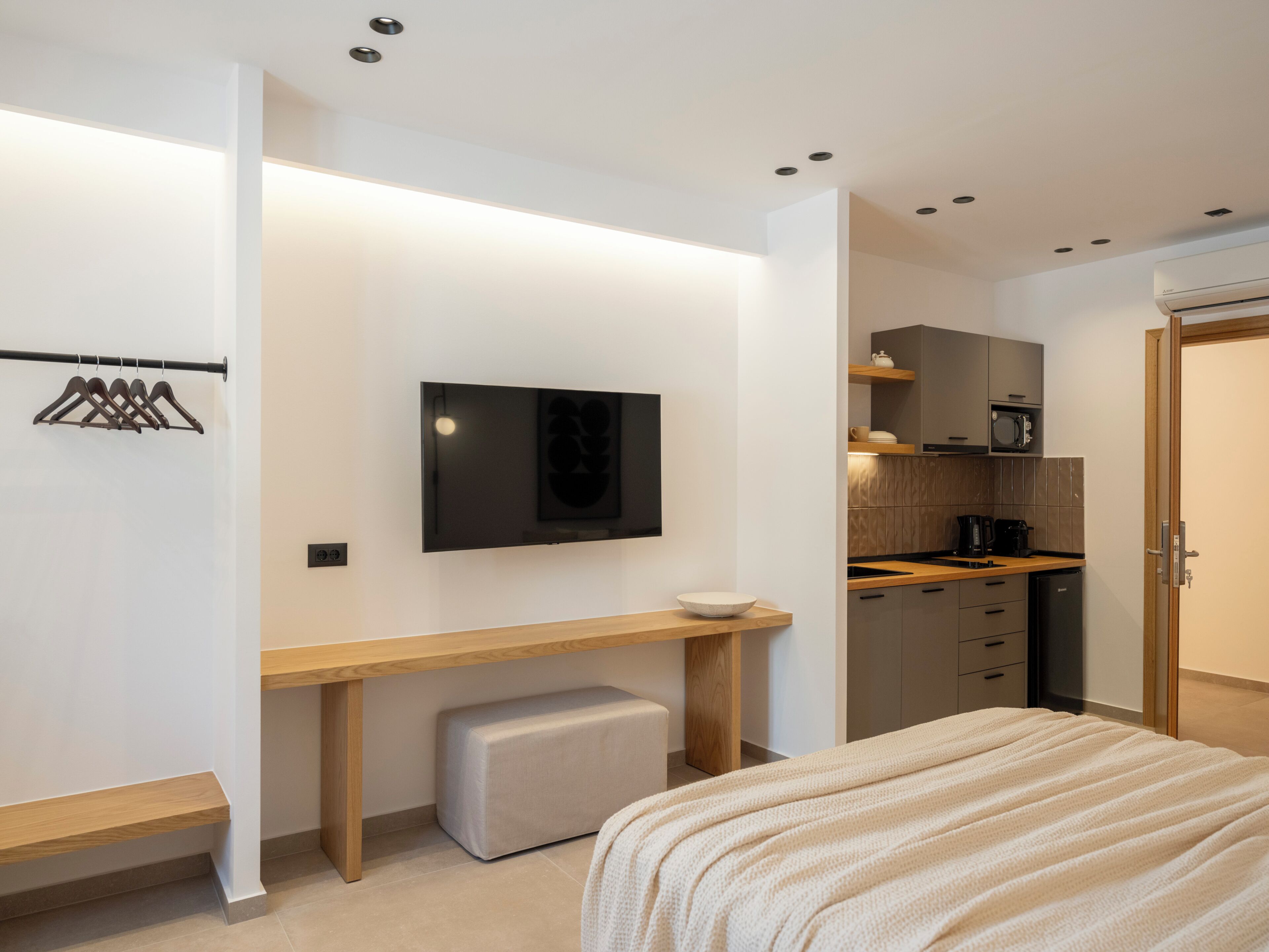 Een moderne slaapkamer met een bed, bureau, televisie en kitchenette.