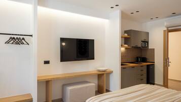 Een moderne slaapkamer met een bed, bureau, televisie en kitchenette.