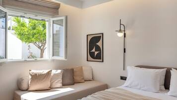 A modern bedroom with a sofa bed, a bedside table, a lamp, and a window with a view of greenery.