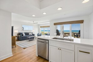 A modern kitchen with a dishwasher, white cabinetry, and a large window overlooking the ocean. - 101 Oceans Of Amelia 2 Bedroom Condo (Fernandina Beach)