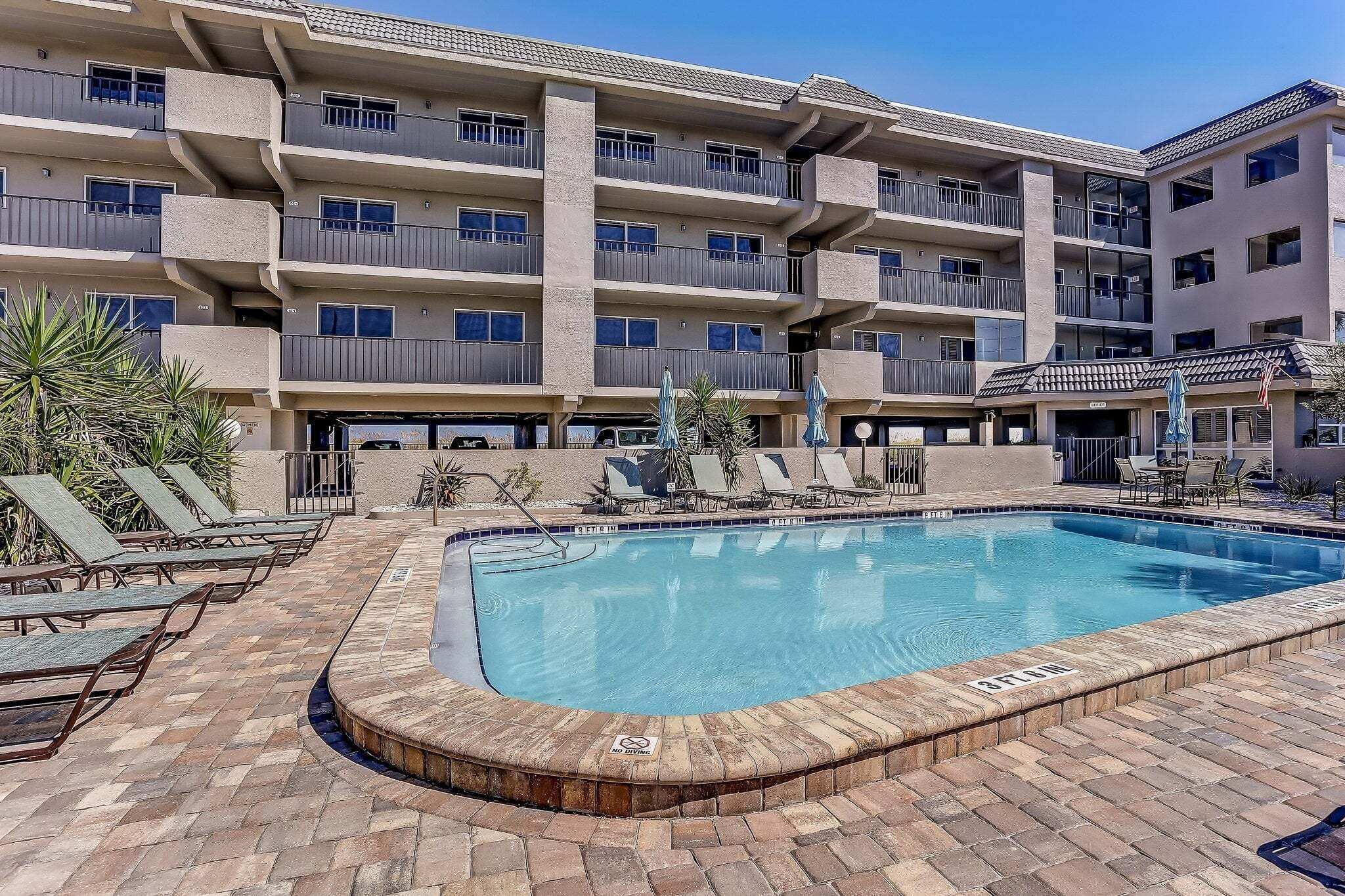 A multi-story hotel with a swimming pool, sun loungers, and a covered patio area.