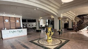 A lobby with a reception desk, a grand staircase, and a decorative fountain.