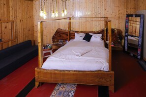 Una cama con dosel de madera con ropa de cama blanca, una mesita de noche con lámpara y un espejo en la pared.