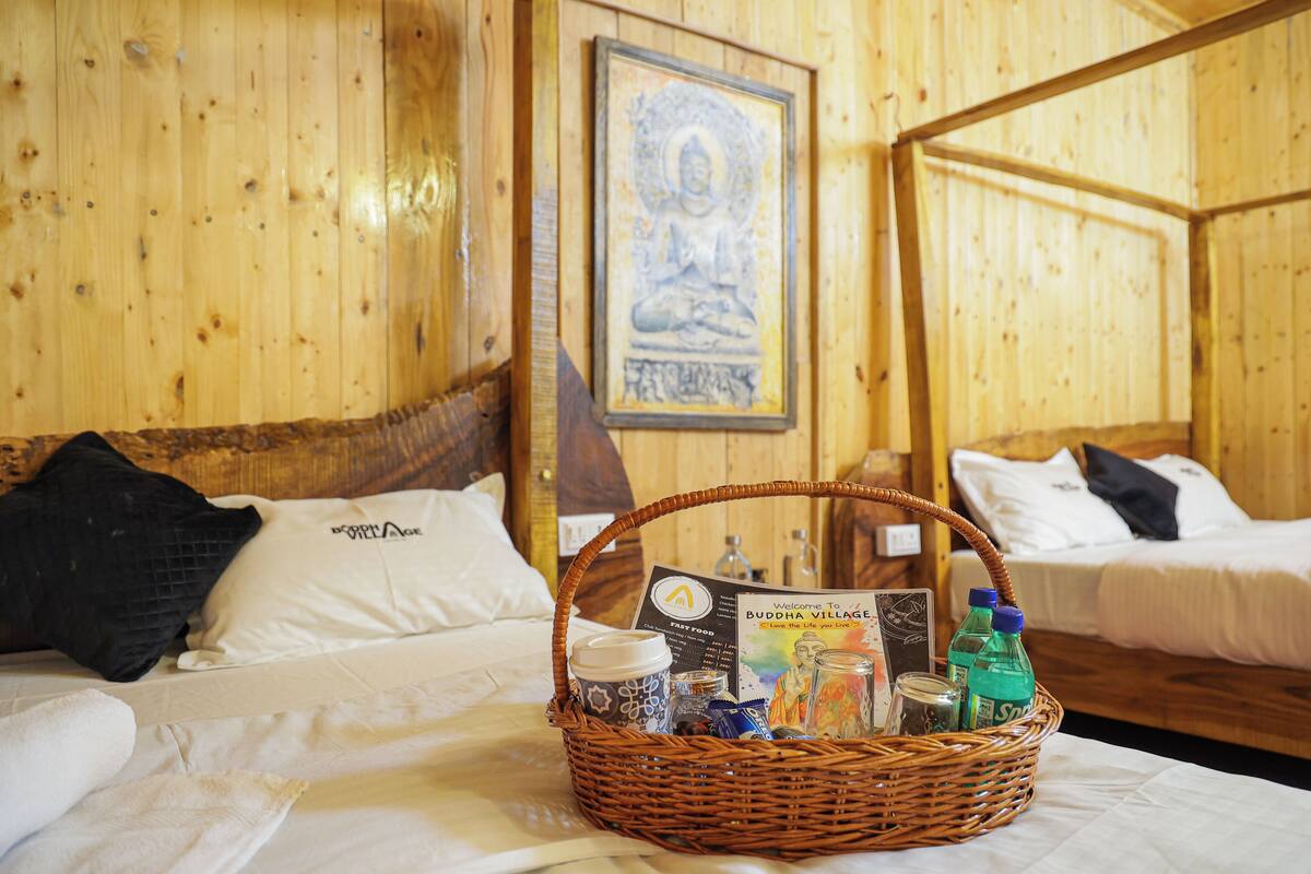 Quarto de madeira com duas camas, uma estátua de Buda emoldurada e um cesto com vários objetos sobre a cama.