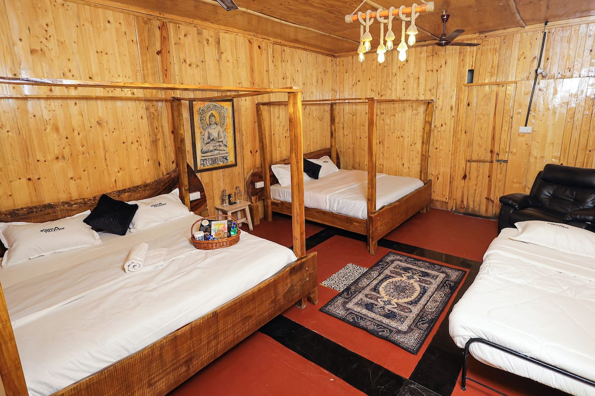 Quarto de madeira com três camas, uma cadeira de massagem, um ventilador de teto e um quadro na parede.
