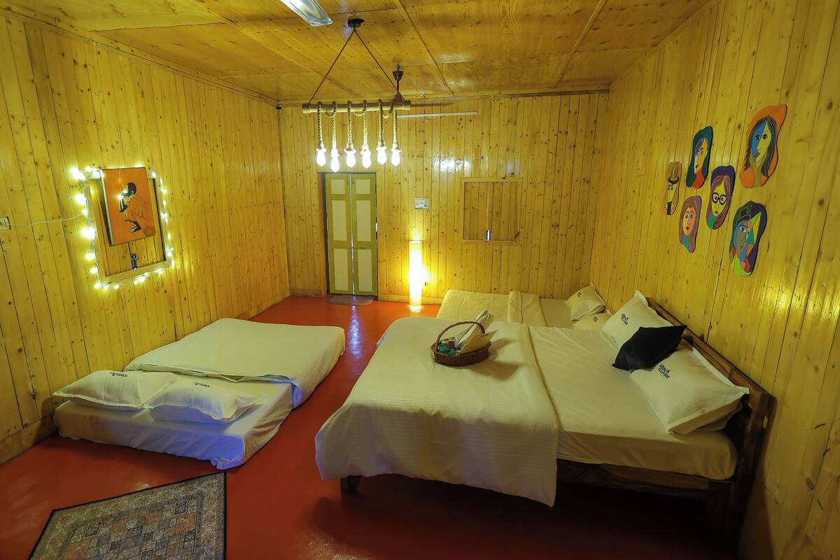 Quarto com duas camas, um espelho iluminado, teto de madeira e uma porta.
