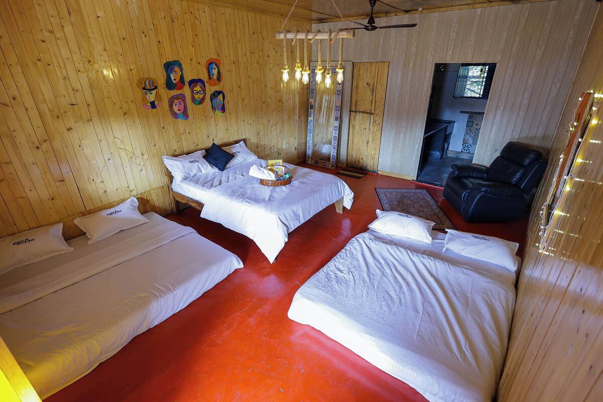 Quarto com duas camas, paredes de madeira, um ventilador de teto e piso vermelho.