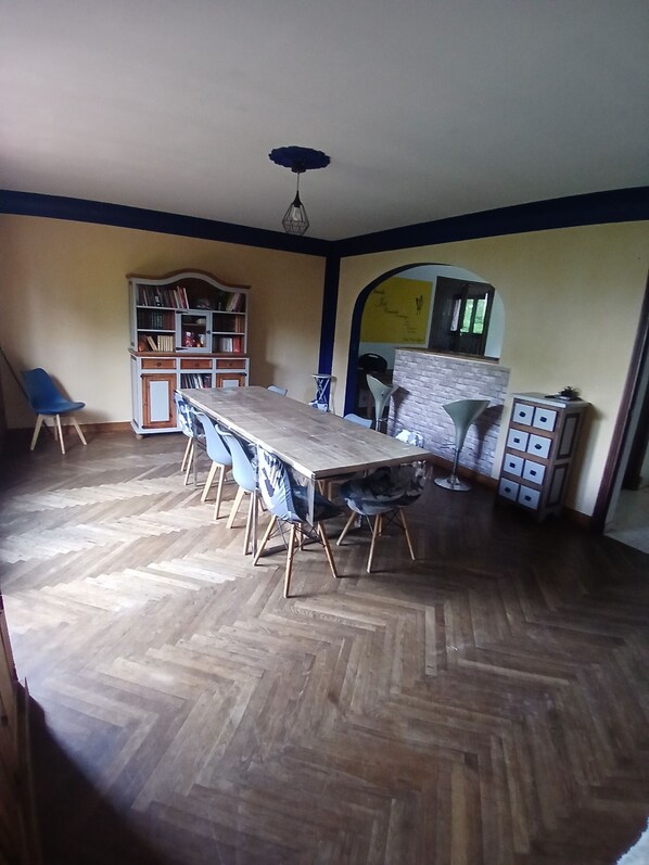 Un espace repas doté d’un parquet en bois disposé en motif à chevrons, d’une longue table avec des chaises, d’une bibliothèque et d’un mur en briques.