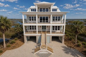 Une maison à plusieurs étages située en bord de mer, dotée d’un escalier central, de balcons et offrant une vue sur l’eau.