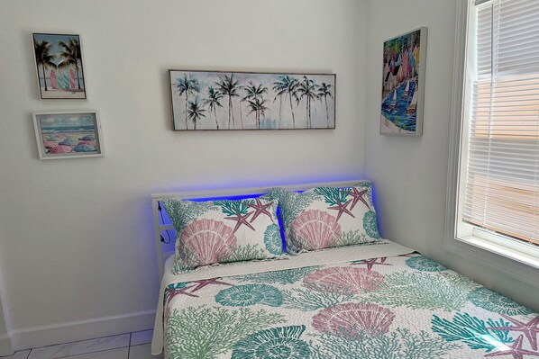 Un dormitorio con cama, decoración en la pared y una ventana con persianas.