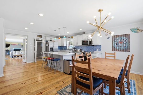 A modern kitchen with white cabinets, a central island, a dining table with chairs, and a unique ceiling light fixture. - 3BR with POOL, Hot Tub, 2 baths, open kitchen, pkg (Rehoboth Beach)