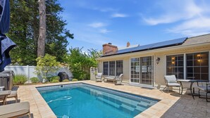Ein rechteckiger Pool mit gefliesten Rändern, umgeben von Terrassenmöbeln und einem überdachten Bereich.