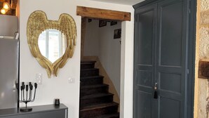 A living room with a black sofa, a heart-shaped mirror, a dark wooden staircase, and a dark blue door. - Charming apartment in the historic center of Montignac-6 people -3 bedrooms (Montignac-Lascaux)