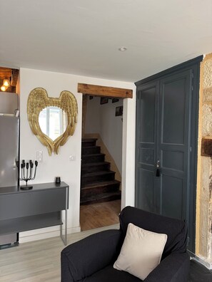 A living room with a black sofa, a heart-shaped mirror, a dark wooden staircase, and a dark blue door. - Charming apartment in the historic center of Montignac-6 people -3 bedrooms (Montignac-Lascaux)
