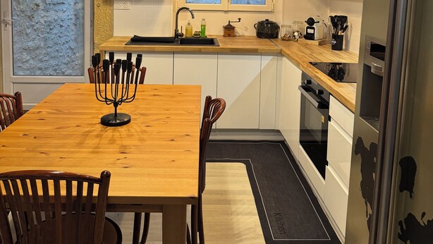 A modern kitchen with wooden beams, a dining table with chairs, a refrigerator, and a window with a view. - Charming apartment in the historic center of Montignac-6 people -3 bedrooms (Montignac-Lascaux)
