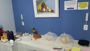 A breakfast buffet setup with a variety of food items, a painting, and informational signs on a blue wall. - Hotel Canedo (Corumbaíba)
