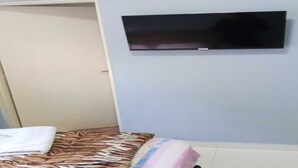 A room with a bed, a television mounted on the wall, and a door. - Hotel Canedo (Corumbaíba)