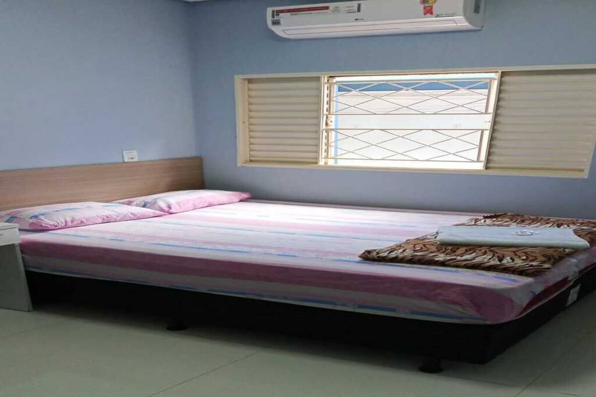 Uma cama de solteiro com cabeceira, mesa de cabeceira e um aparelho de ar condicionado acima da janela.