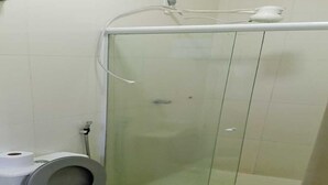 A bathroom with a toilet, a glass shower enclosure, and a visible pipe. - Hotel Canedo (Corumbaíba)