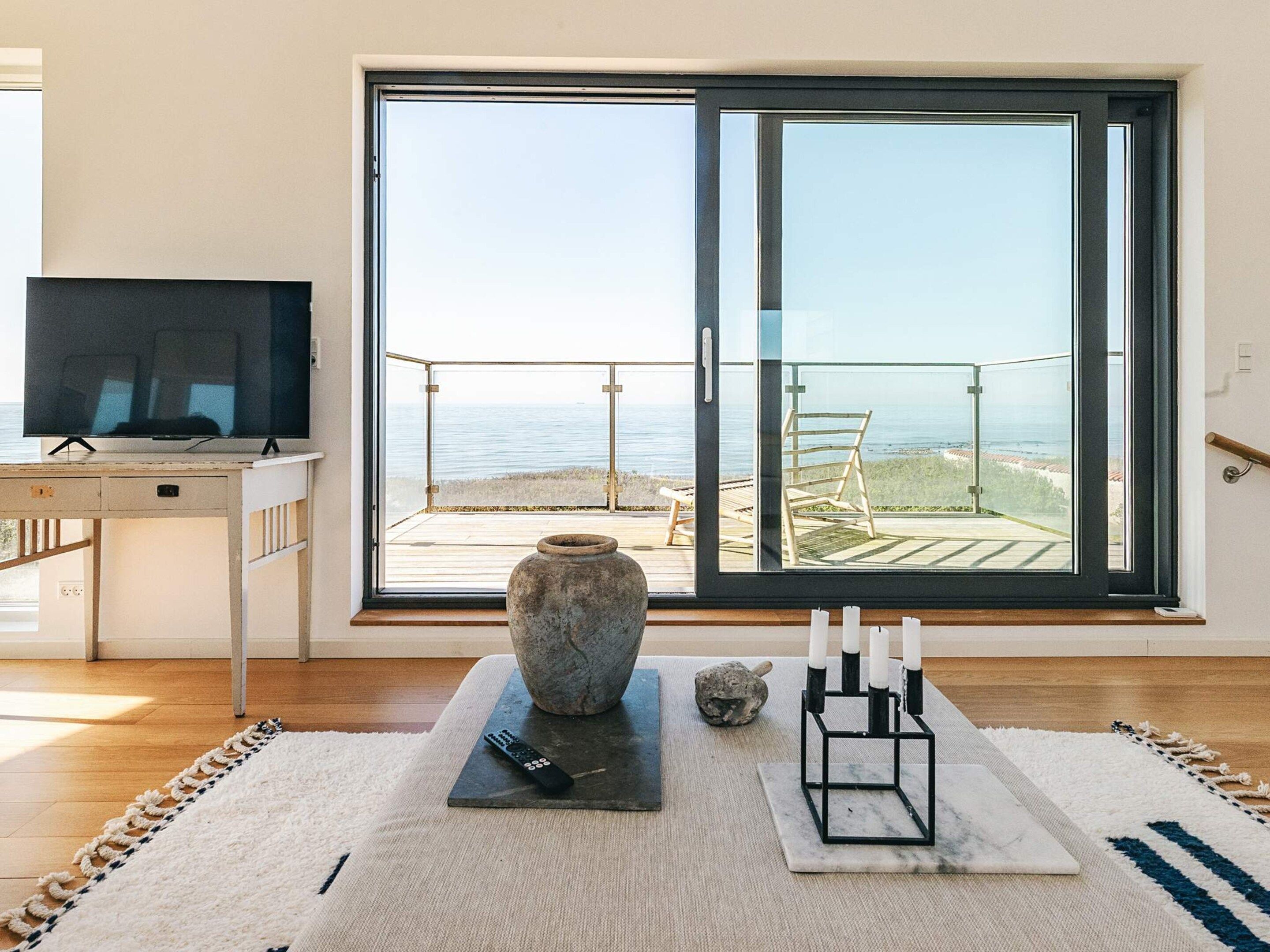 Una habitación con televisión, un jarrón de piedra, un control remoto y velas sobre una alfombra.