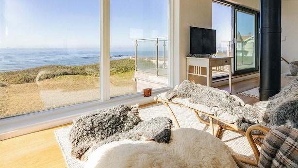 A room with a large window overlooking the sea, a fireplace, and a television on a stand. - 5 Star Holiday Home in Vejby (Vejby)