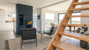 A modern interior with a stone fireplace, a wooden staircase, and a view of the outdoors. - 5 Star Holiday Home in Vejby (Vejby)