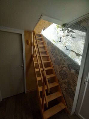Un escalier en bois menant à une mezzanine, agrémentée d’un rideau à motifs et d’une petite plante.