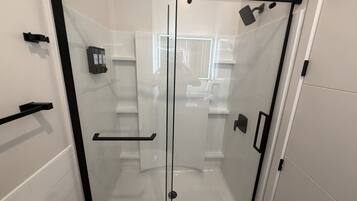 A glass-enclosed shower stall with a black frame, a white tiled wall, and a black towel rack.