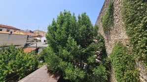 Une ruelle étroite, bordée d’un côté par un mur de pierre et avec un arbre au centre.